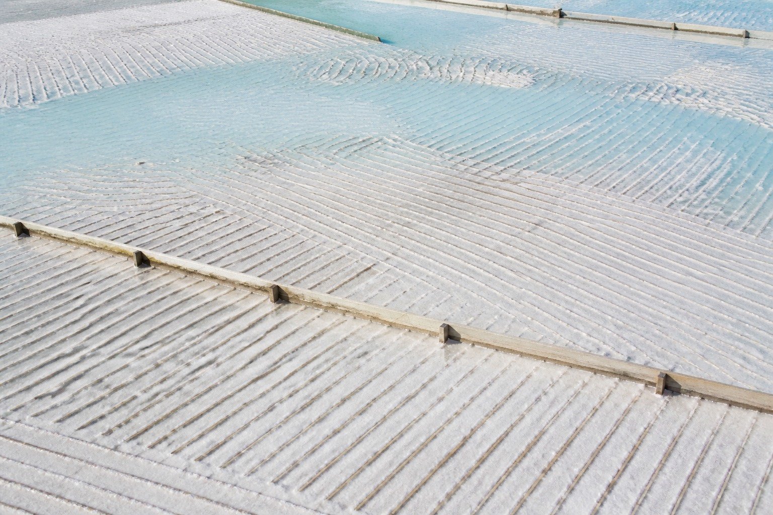 Thin rake lines across a pale salt crust and shallow turquoise film